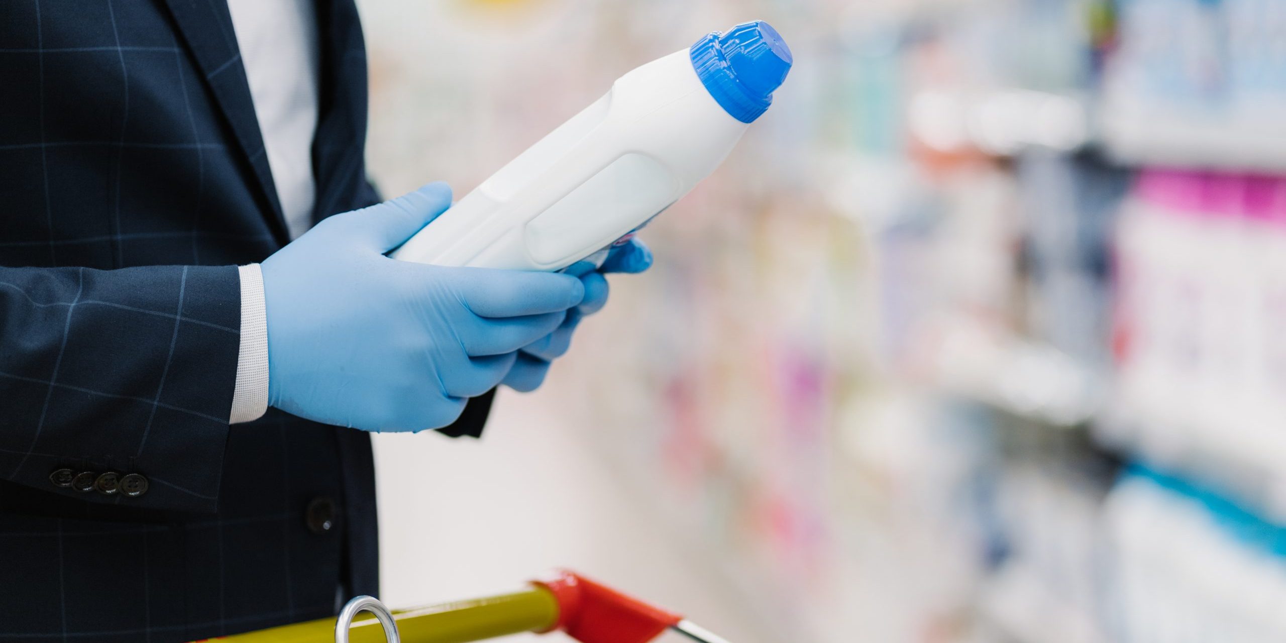 Man chooses detergent in household goods store, holds bottle with liquid powder, wears medical gloves to protect from coronavirus, reads product information. Making shopping during quarantine